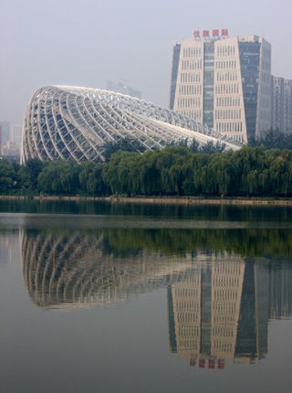 View from across the water of the curved, irregular shaped Phoenix TV building framework. There are trees and other buildings nearby