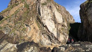 A large rock outcropping with two people walking along the bottom