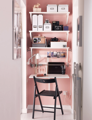 Drop down desk in a narrow landing with a pink statement wall, a black chair and shelves with plenty of folders and essentials on them
