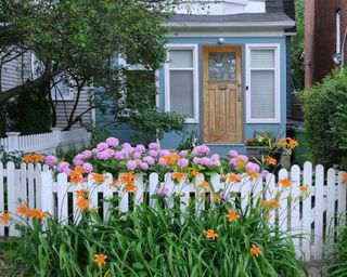 Charming small old house with white picket fence and flowers in front garden