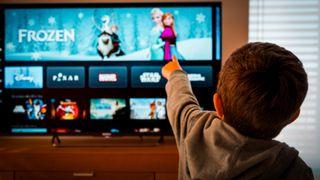 A young boy pointing at a TV showing Disney Plus