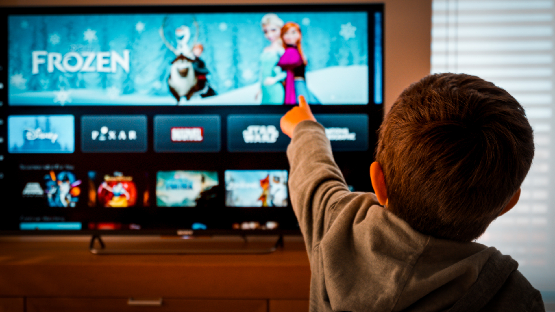 Seorang anak laki-laki menunjuk ke TV yang menayangkan Disney Plus