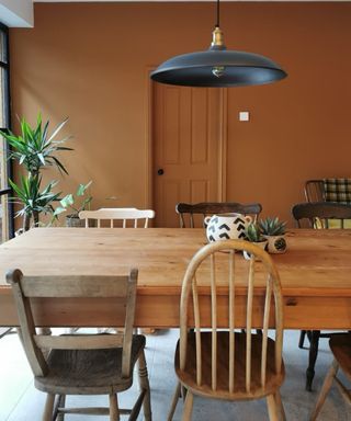 dining room with dark orange wall, wood dining table and mix of farmhouse dining chairs