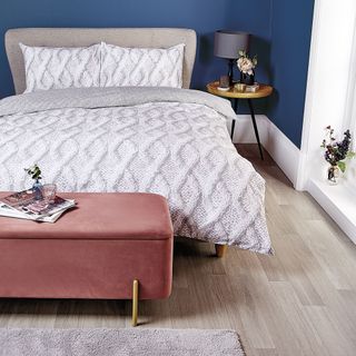 Aldi ottoman in plum coloured velvet in front of a bed with arran knit patterned duvet cover