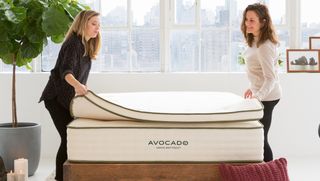 Two women placing an Avocado mattress topper on an Avocado mattress