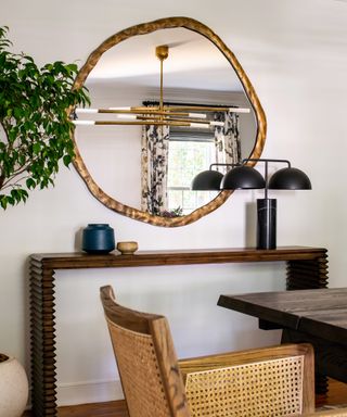 A white dining room with a large circular gold table hung over a dark wooden console table