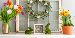 Easter mantel decor showing jugs of tulips, faux grass rabbits and a central Hello Spring sign