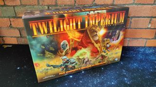 Twilight Imperium box on a starry surface, against a brick background