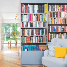 Hallway with storage and bookcase and doors painted in duck egg blue, with staircase opposite with grey stair carpet and yellow and orange painted bannisters.