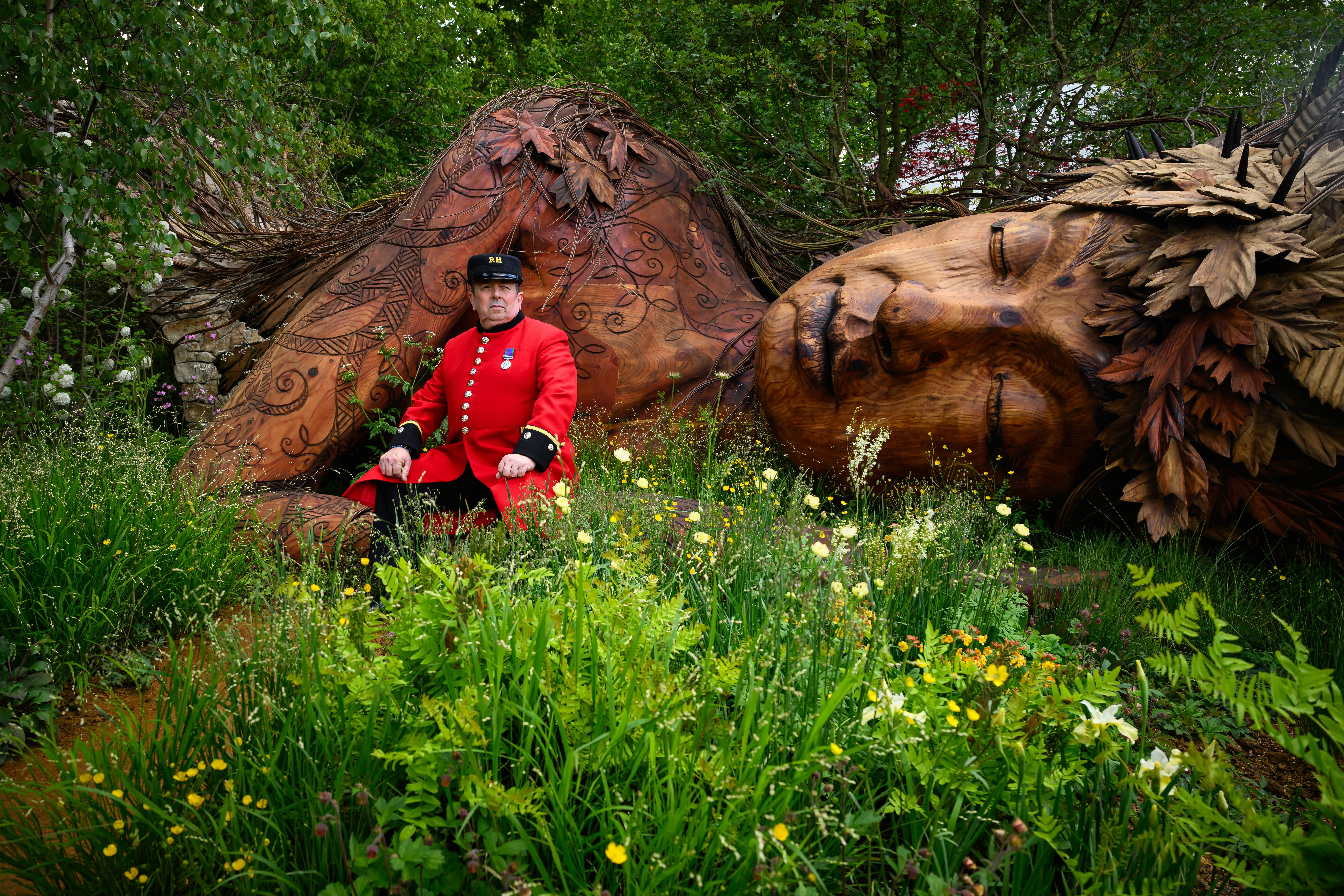 LONDON, ENGLAND - MAY 18: A man wearing the traditional scarlet uniform of the Chelsea pensioners sits among the flowers of the "The Campaign to Protect Rural England Garden: On The Edge" garden