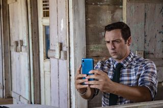 DI Neville Parker (Ralf Little) sits outside his beach hut with his phone in his hand, awkwardly attempting to take a selfie