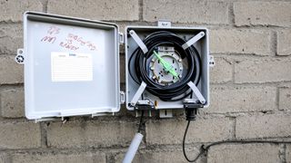 A fiber optic cable going into the back of a house with the excess cable in a metal box