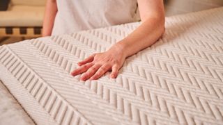 A hand and forearm rest on the surface of the Leesa Legend Hybrid Mattress, testing the temperature regulation and pressure relief