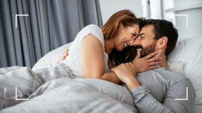 Woman and man lying in bed together laughing and smiling under the covers, representing how to spice things up in the bedroom