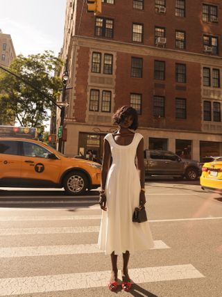 Model and fashion influencer Amy Julliette Lefévre on the street in New York City with yellow cabs in the background wearing a white summer dress and bright red flat shoes.