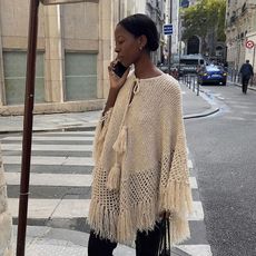 A Parisian woman wearing a knit poncho, black capri pants, and heels
