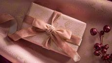 A gift wrapped in pink wrapping paper with gold dotted stars and a velvet ribbon beside a red berry twig