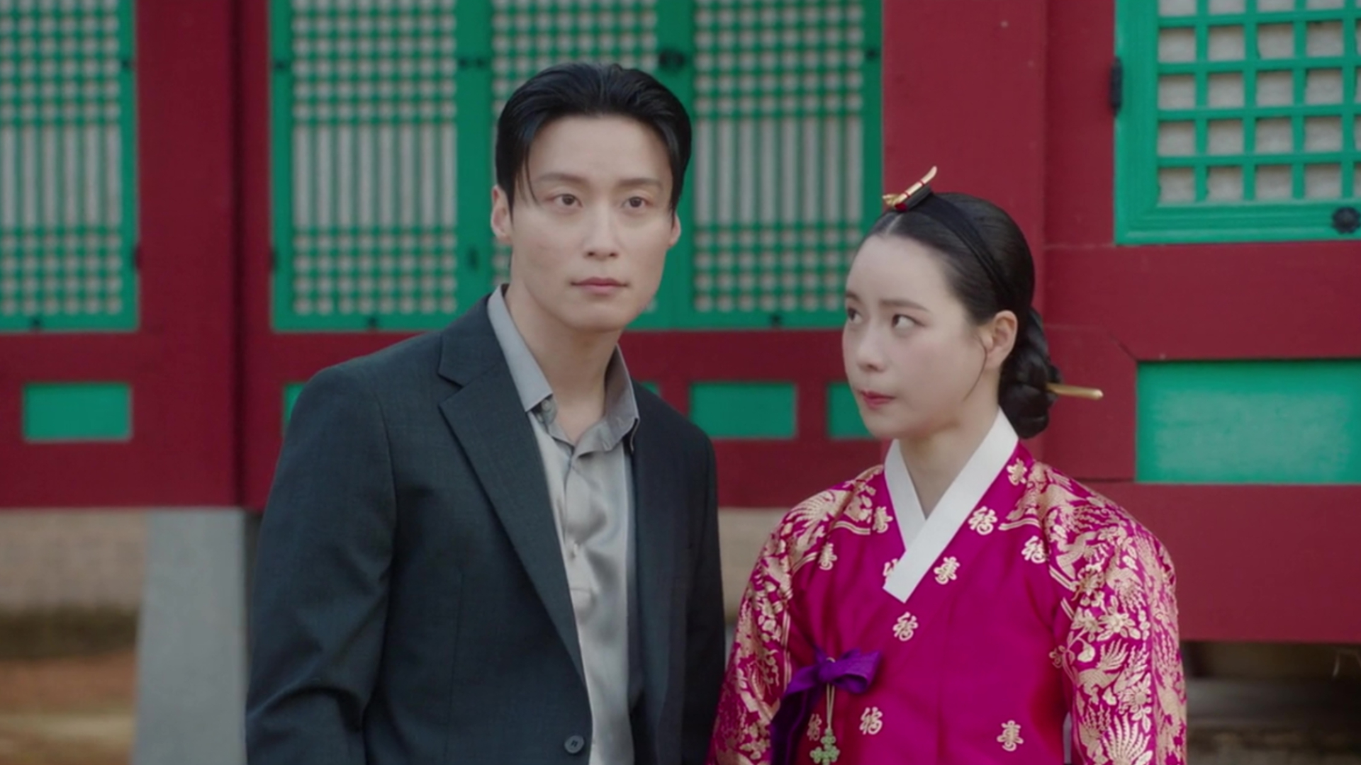 A Korean man in a suit (Heo Nam-jun as Cha Se-gye) and a Korean woman in traditional clothing (Lim Ji-yeon as Shin Seo-ri) stand in front of a traditional palace in 'My Royal Nemesis'.