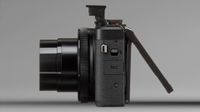 Side view of a black digital camera with lens extended and flip-out LCD screen opened
