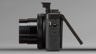 Side view of a black digital camera with lens extended and flip-out LCD screen opened