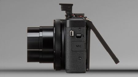 Side view of a black digital camera with lens extended and flip-out LCD screen opened