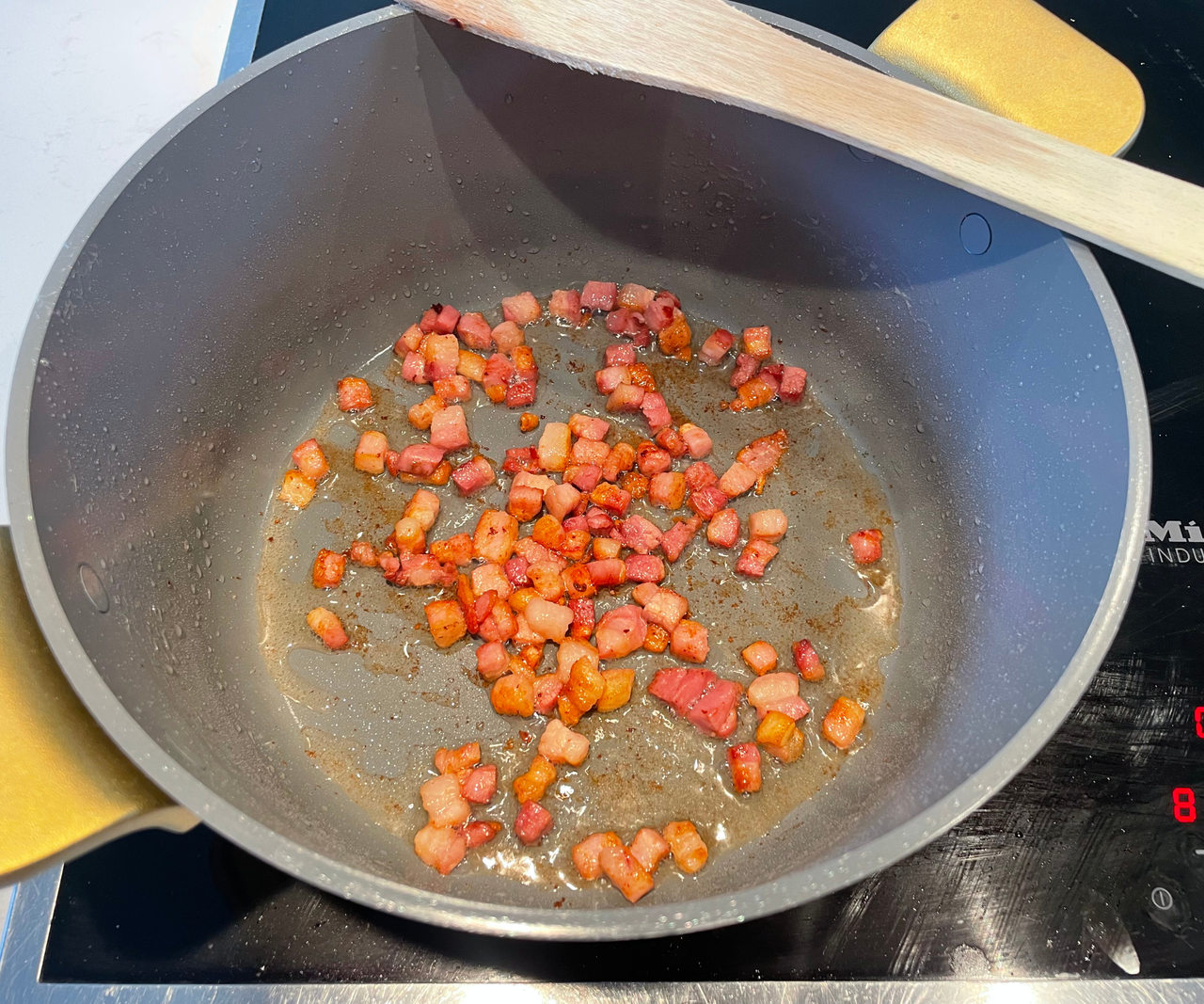 Chopped peppers frying in a blue ceramic dutch oven on an electric stove, with a wooden spoon balancing on the edge of the rim.