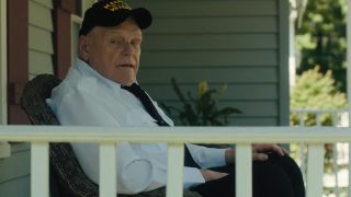 Brian Dennehy wearing a Navy cap and sitting on a porch