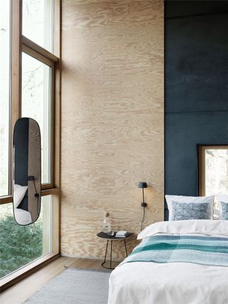A plywood statement wall and bed next to a large floor-to-ceiling window.