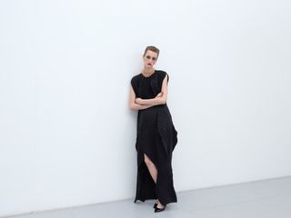 Woman in black Issey Miyake dress leaning against wall