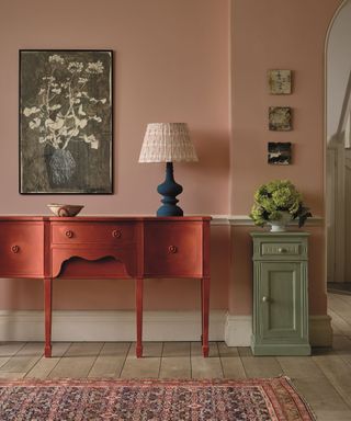 A pink entryway with a red console table and floral wall art