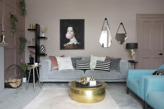 Plaster pink painted living room with grey carpet, pink rug, grey and blue sofas, brass coffee table, large statement artwork and two geometric mirrors
