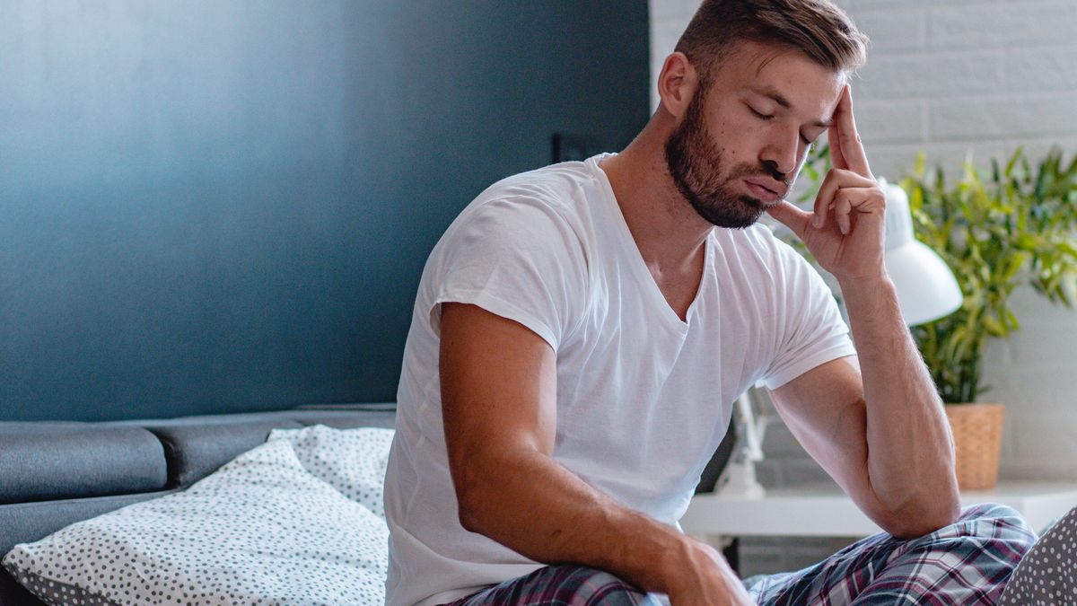 A man sits up in bed because he feels too hot to sleep