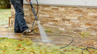 Person using a pressure washer to clean patio next to a patch of grass.