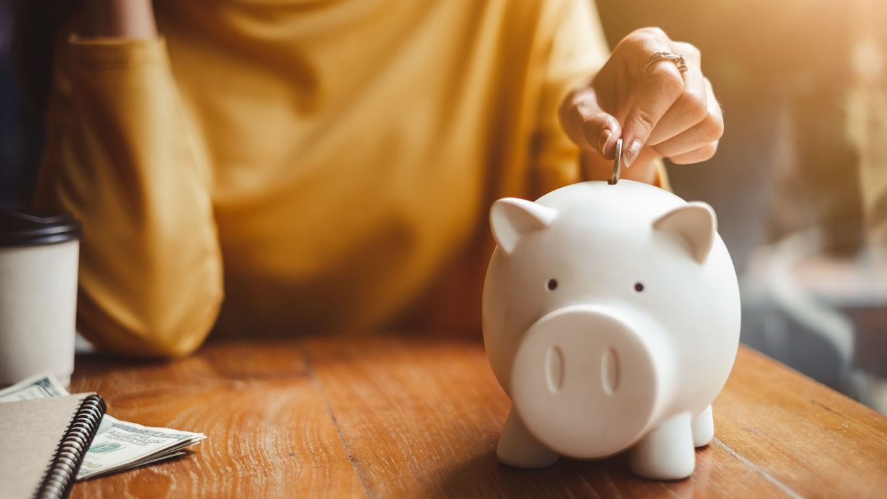 A woman puts a coin into a piggy bank.