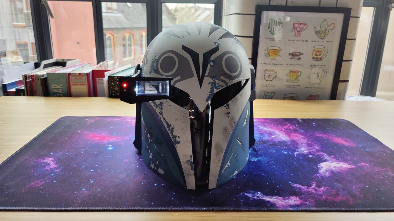 Black Series Bo-Katan Helmet with heads-up display down and lit up. The helmet is facing forward. There is a gray, black, and white owl-like pattern on the light blue helmet and a black T-shaped visor.