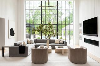 Living room with large black-framed glazing, grey sofa and armchairs, neutral rug and white and black wall art