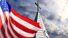 An American flag flies near a church steeple with a cross on top.