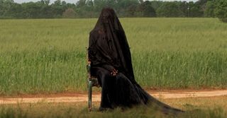 a woman in a black dress and shall sits outside of a field in a chair in a still from the woman in the yard