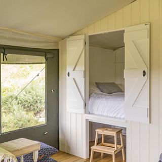 Inside luxury tent with canvas walls, bed in cupboard and a wooden table