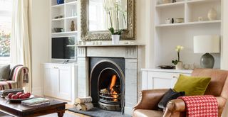 cream living room with open fire, bespoke built-in alcove shelves and a leather armchair