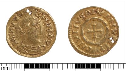 A close up of a small golden coin, its two faces side by side against a white background with a millimeter ruler below with black and white tick marks.