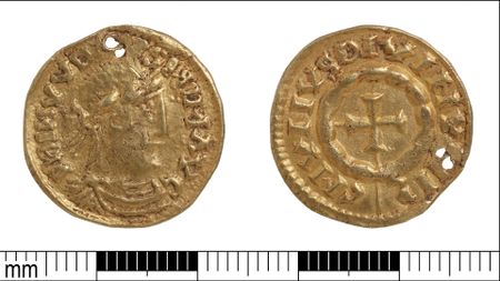 A close up of a small golden coin, its two faces side by side against a white background with a millimeter ruler below with black and white tick marks.