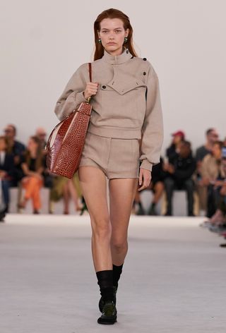 model wearing stylish outfit with socks, including a tan coat with matching shorts and black socks and sneakers