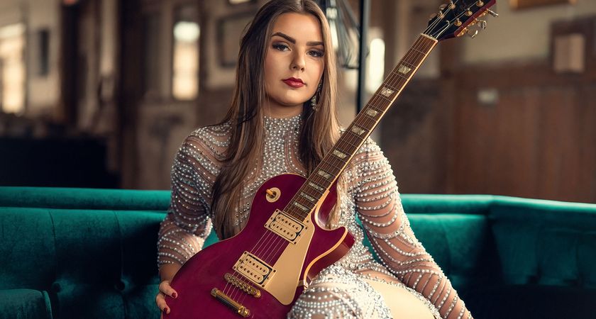 Ally Venable sits on a teal sofa with a pink-purple Les Paul 