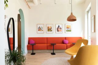 brightly coloured waiting room with orange cushioned bench, yellow chair and small black tables