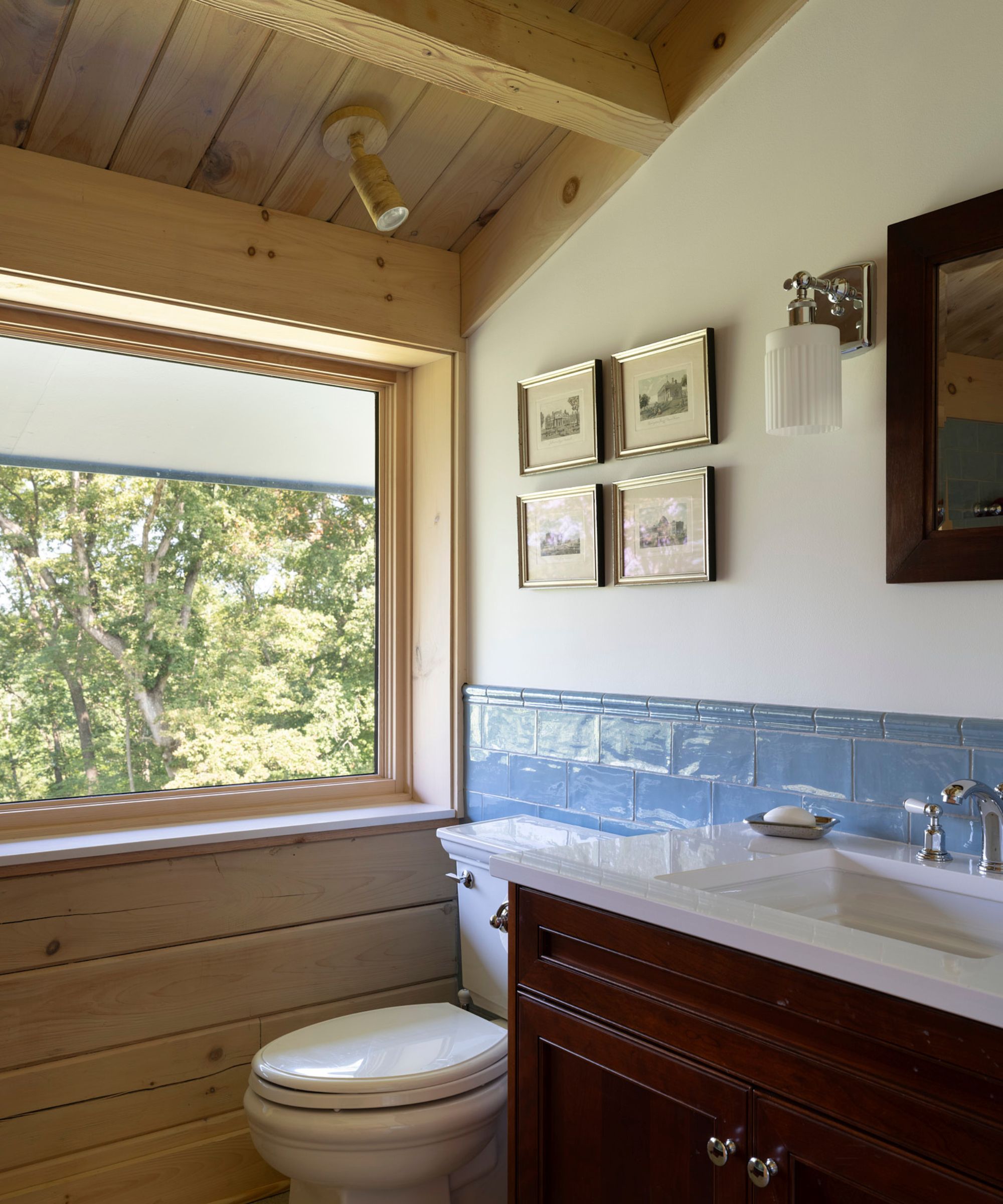 A modern bathroom with a white wall, a wood-clad wall and sloped ceiling, a dark wood sink vanity, and blue tiles on the lower wall.
