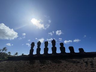 series of moai statues with the sun in the background.