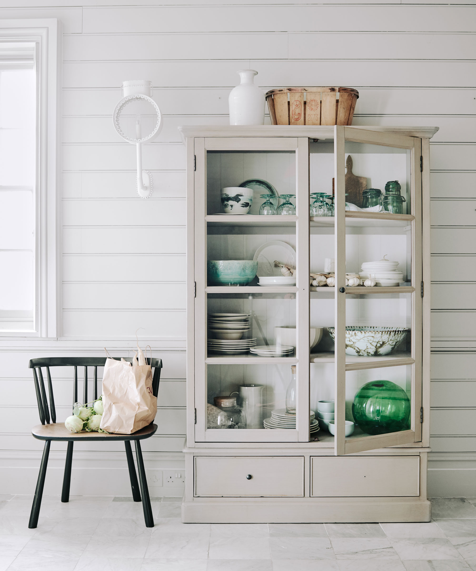 nautical glass fronted dresser in front of white tongue and groove panelling with colour pops of green