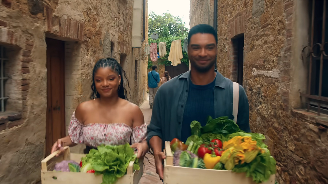 You, Me &amp; Tuscany scene featuring Halle Bailey in a pink dress and Rege-Jean Page in an open button down walking with vegetables.