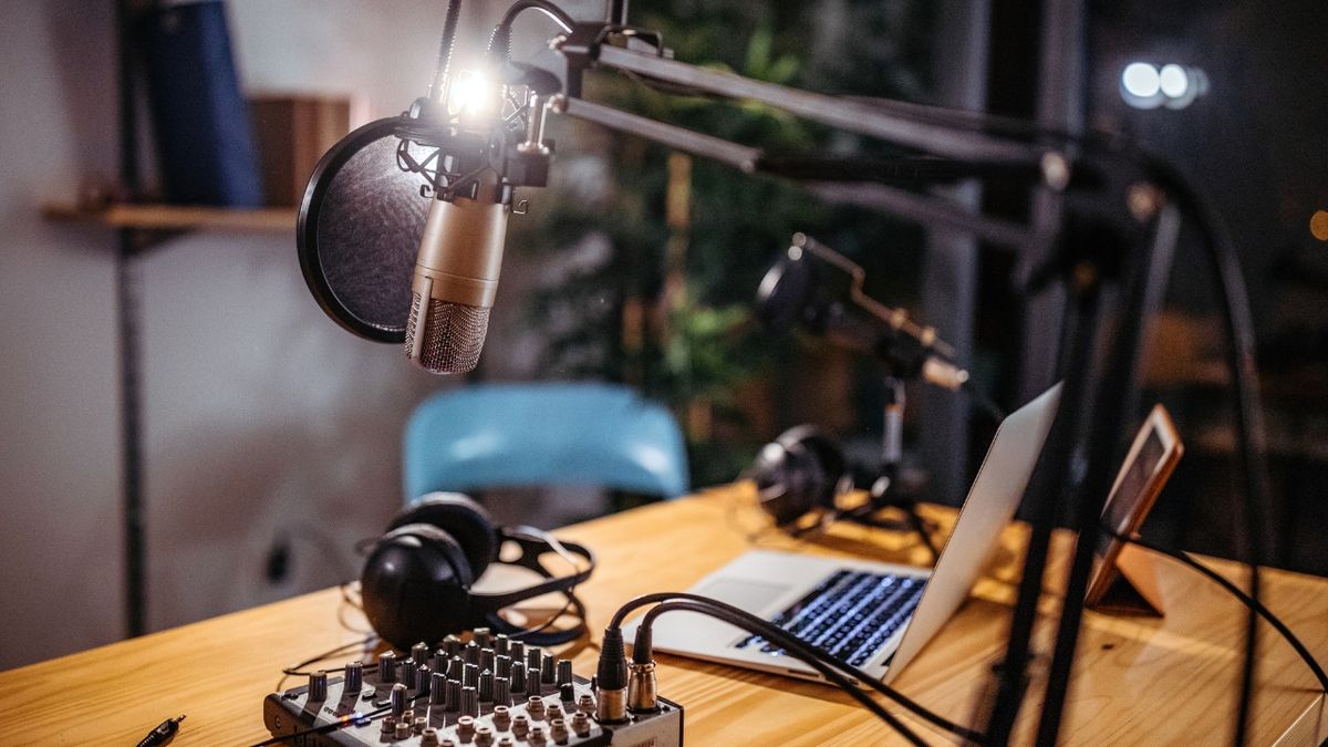 An image of a podcast studio with headphones, mixer, laptop, and condenser microphone